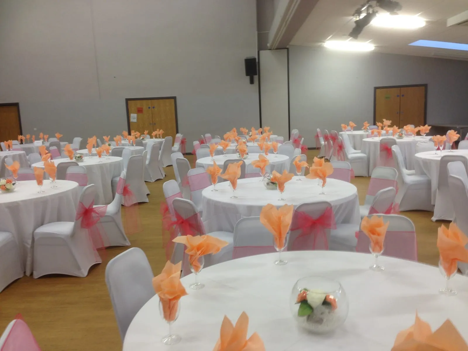 Round tables in white with pink chair sashes and peach napkins folded into glasses at every place.