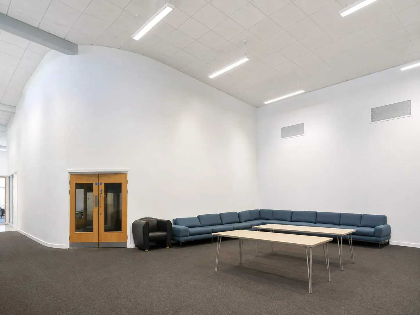 The foyer: a tall, bright entrance space with a curved white wall, grey carpet, a long blue corner sofa and two low tables.