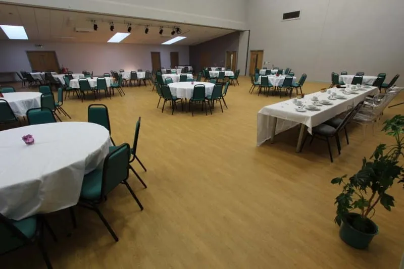 Round tables laid with white cloths and place settings, with a long buffet table running down one side of the hall.