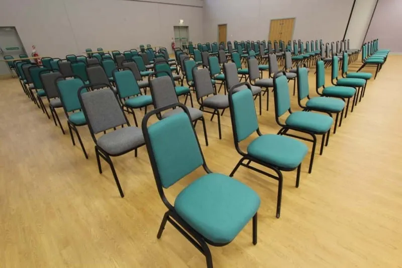Close rows of teal and grey banqueting chairs filling the hall floor, set for a large audience.