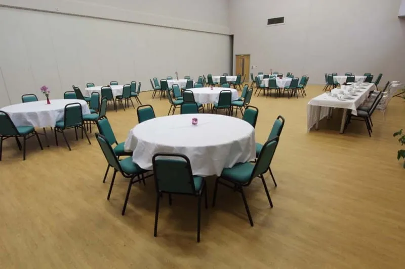 Round tables with white cloths and green chairs spread across the hall, with a long buffet table at the side.