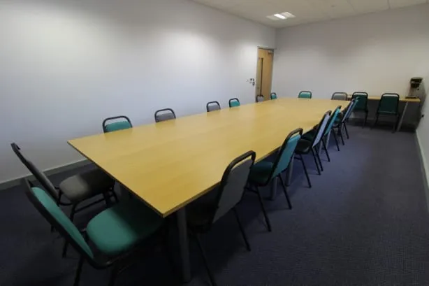 A carpeted meeting room with one long table and around sixteen chairs arranged boardroom style.
