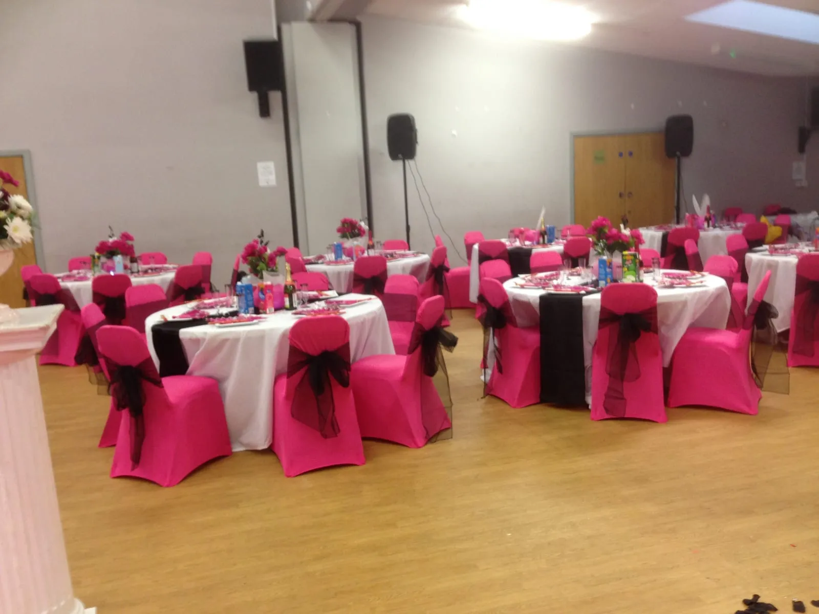 Round tables with white cloths, bright pink chair covers and black sashes, laid for a children's party.