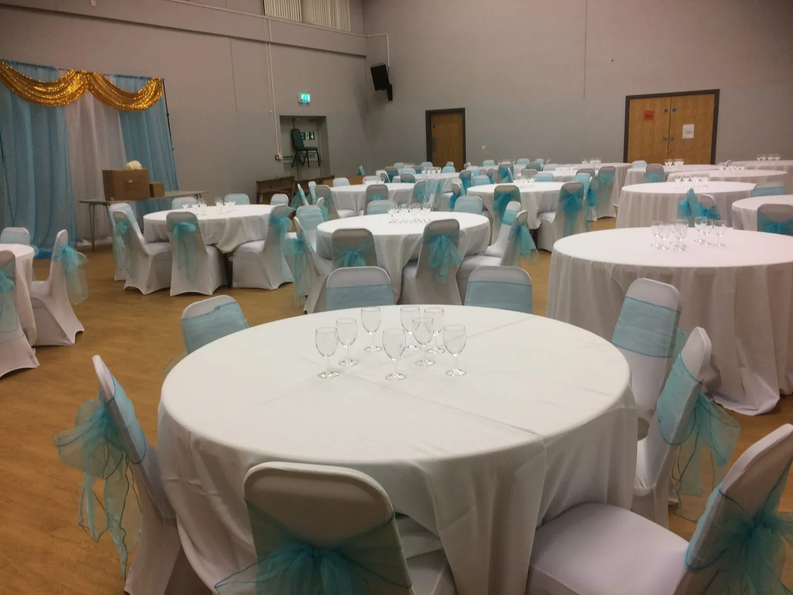 Round tables in white linen with teal organza chair sashes and rows of wine glasses, ready for guests.